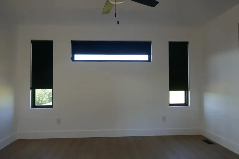 Three black blackout roller shades lowered over a transom and two side windows in an empty room