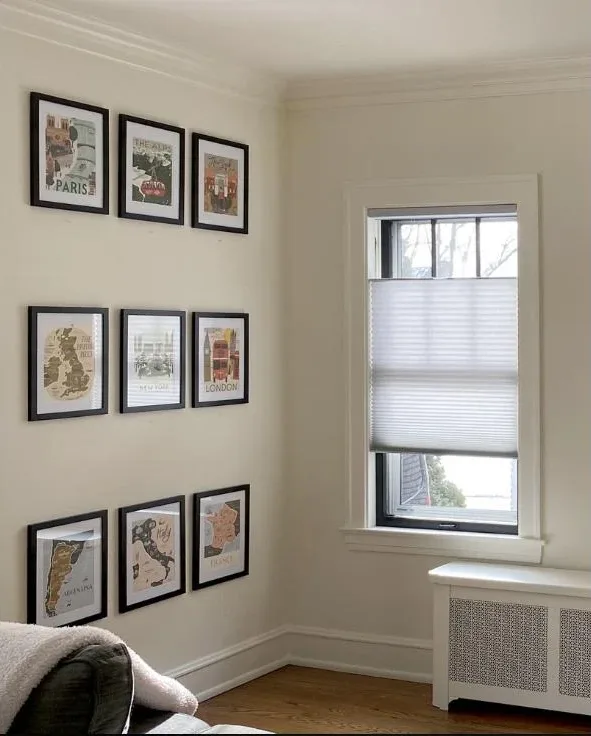 Cellular shade raised from the bottom on a small window beside a framed gallery wall