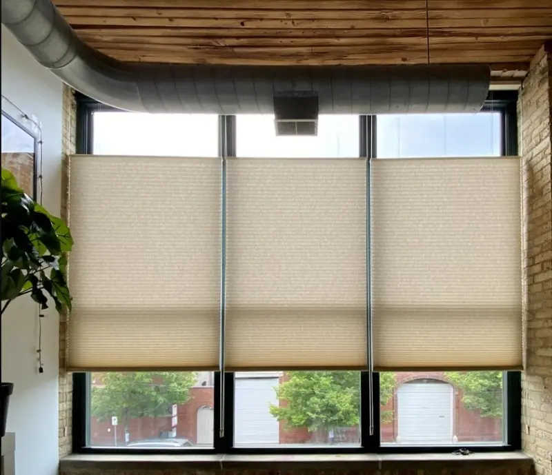 Beige top-down bottom-up cellular shades on tall loft windows with exposed brick