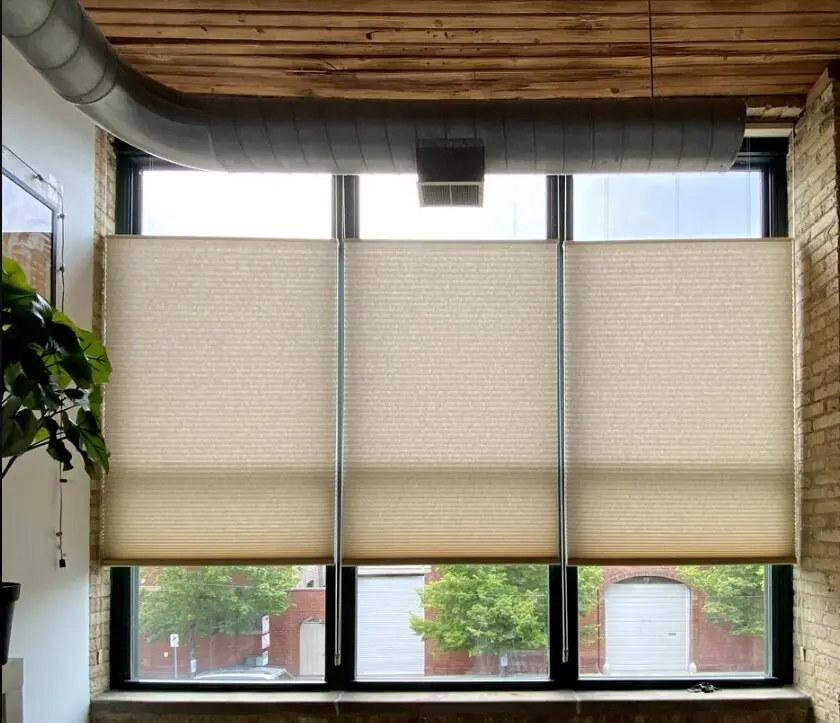 Beige top-down bottom-up cellular shades on tall loft windows with exposed brick