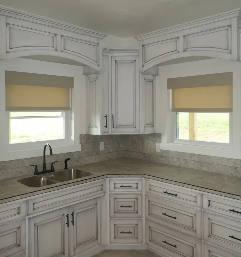 Cream light-filtering roller shades over two corner kitchen windows above a granite counter