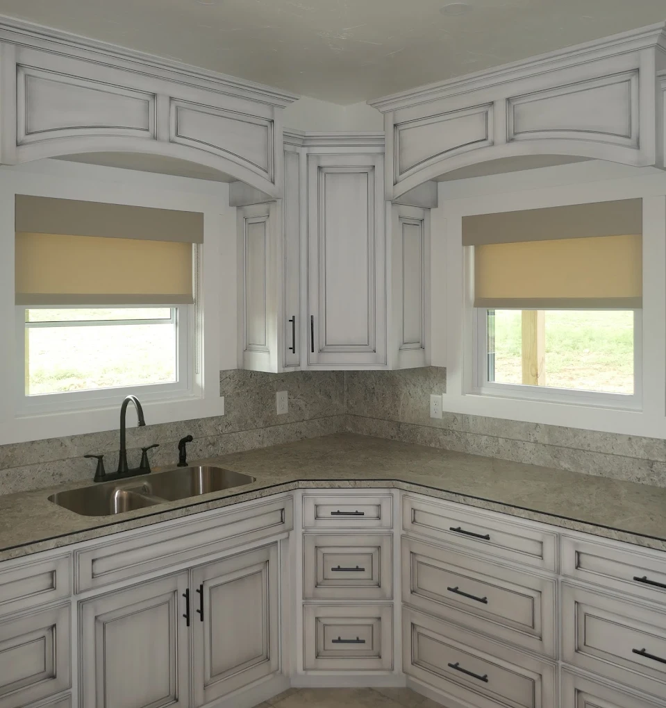 Cream light-filtering roller shades over two corner kitchen windows above a granite counter