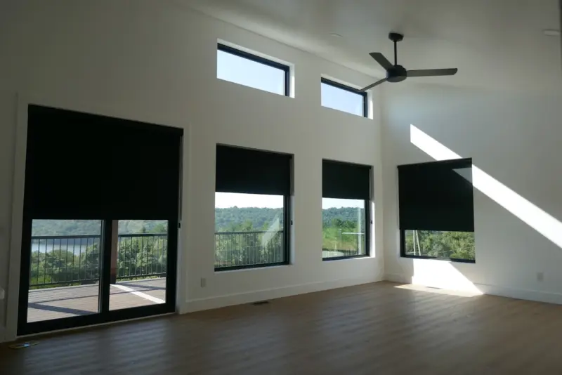 Dark blackout roller shades on five windows of a modern living room with a ceiling fan