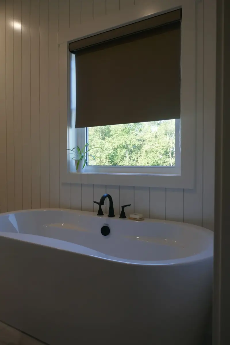 Dark roller shade over a bathroom window above a freestanding tub, shiplap walls