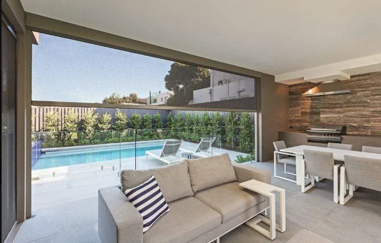 Exterior shades lowered on a covered patio with an outdoor sofa beside a pool