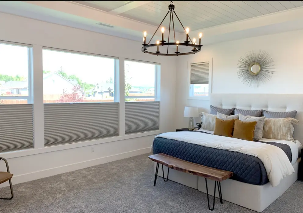 Grey cellular shades set half-height on three bedroom windows beside an upholstered bed