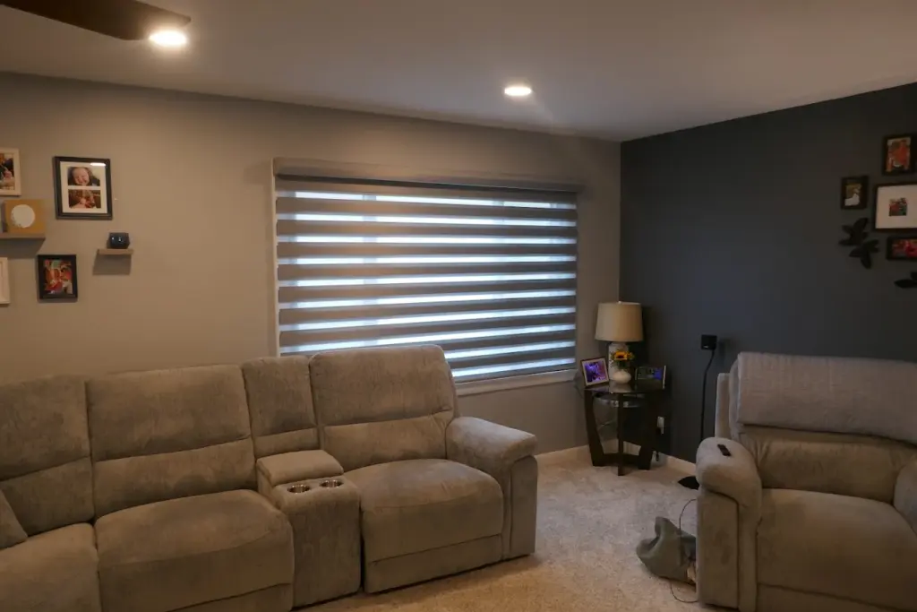 Grey zebra shade with bands aligned for light on a wide family room window above a sectional