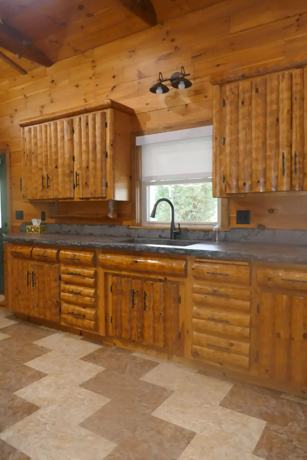 White roller shade over a sink window in a log cabin kitchen