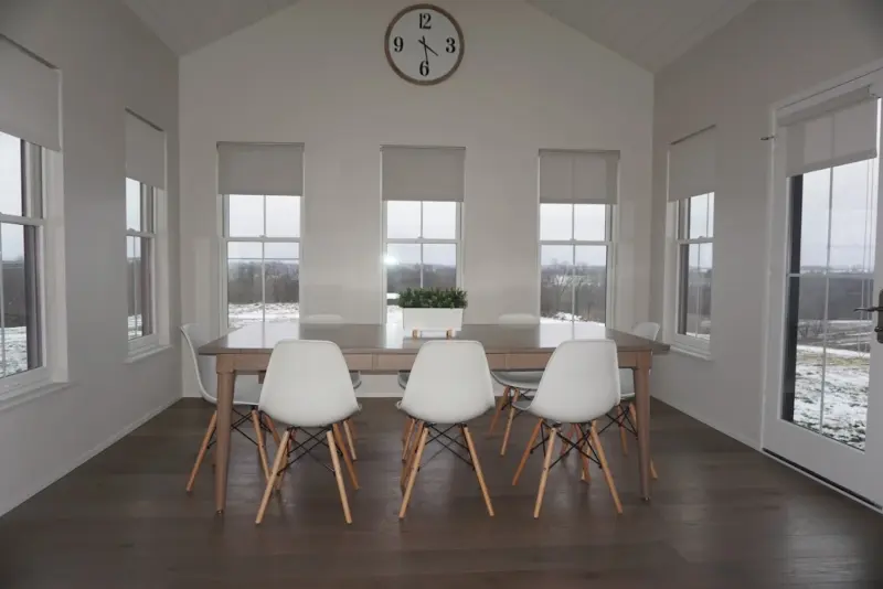 White roller shades on four sunroom windows and a door around a dining table