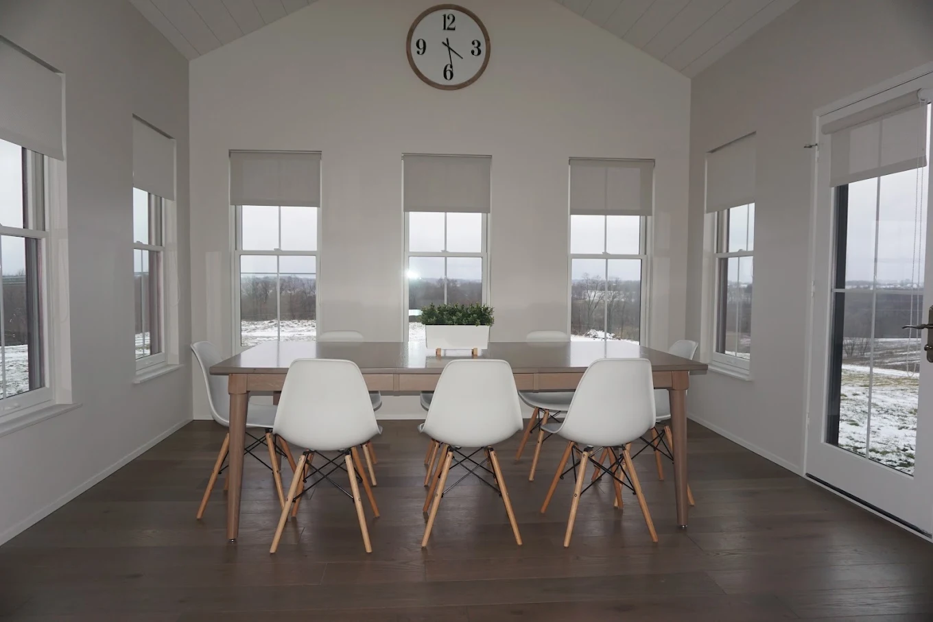 White roller shades on four sunroom windows and a door around a dining table