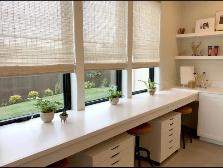 Woven wood shades on three windows above a long white home office desk