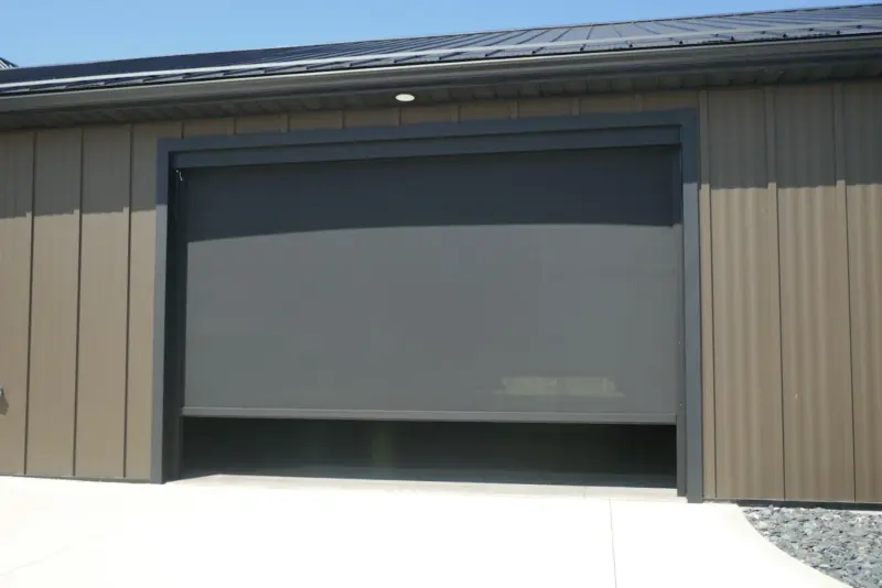 Zipscreen exterior screen fully lowered across a garage door opening on a metal-sided building